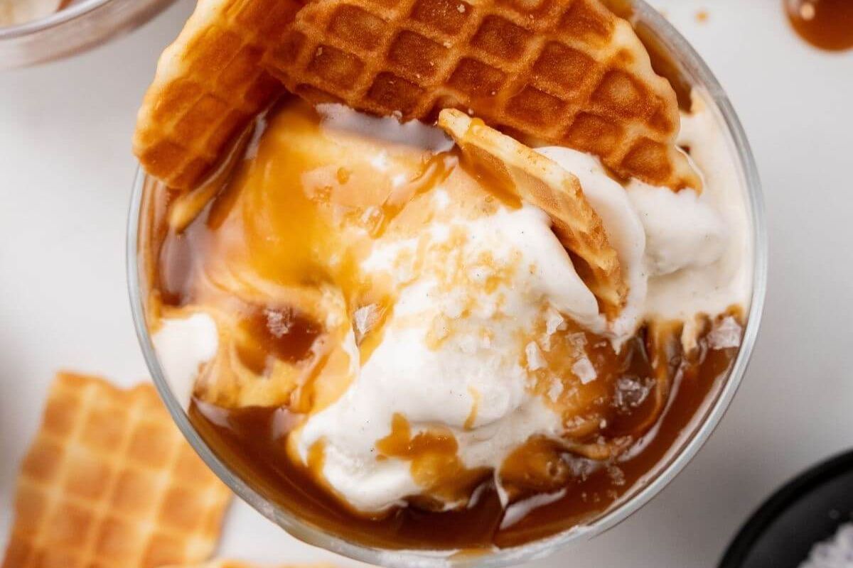 A glass filled with vanilla ice cream, topped with caramel sauce and pieces of waffle.