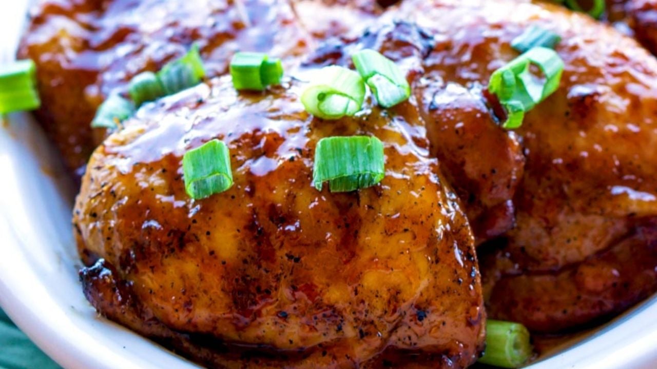 Close-up of glazed, cooked chicken thighs garnished with chopped green onions on a white plate.