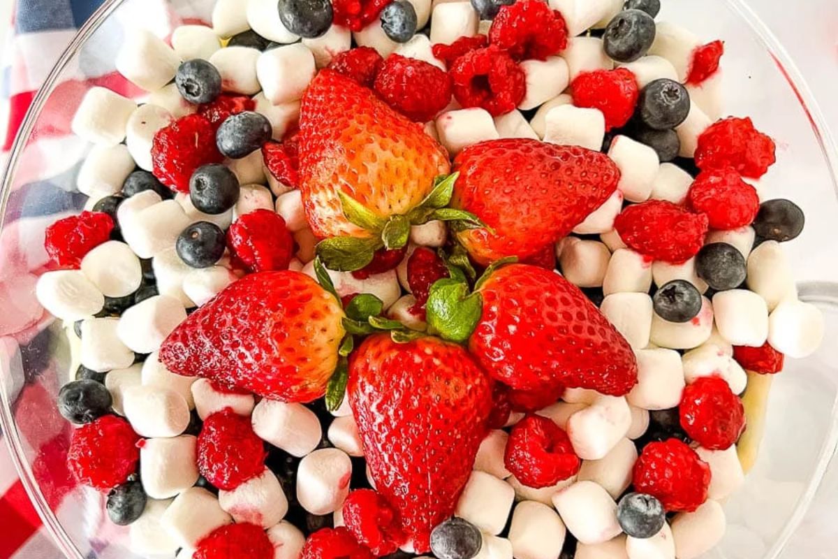 A bowl containing fresh strawberries, blueberries, raspberries, and mini marshmallows arranged together.