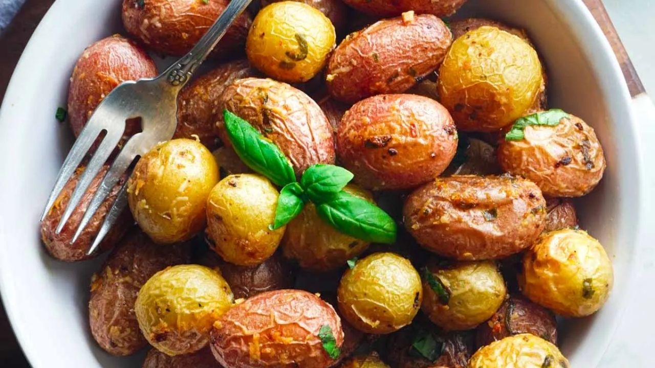 A bowl of roasted baby potatoes garnished with fresh basil, with a fork resting on the side.
