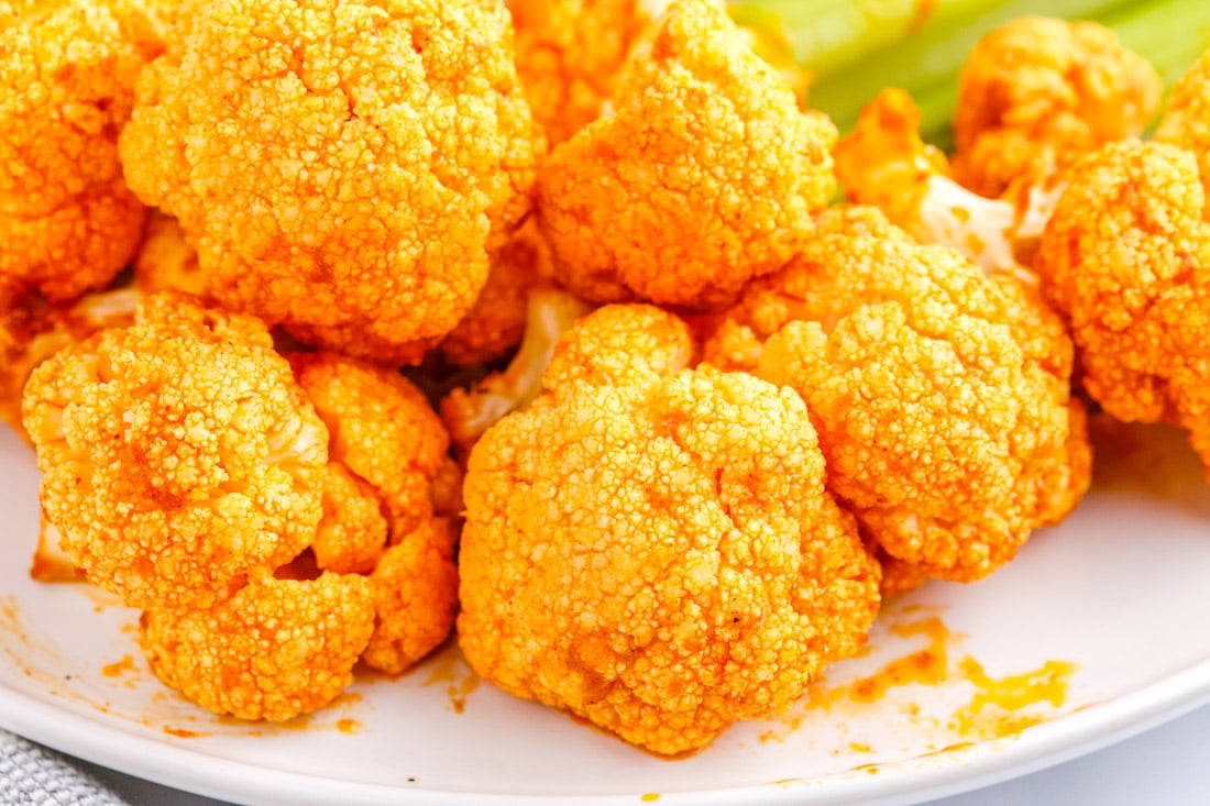Several pieces of cauliflower covered in a bright orange sauce are arranged on a white plate.