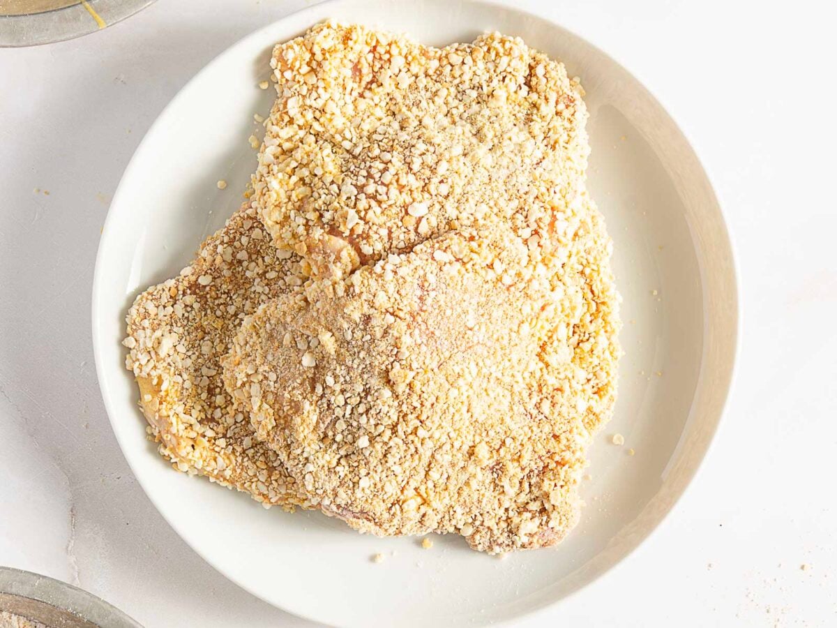 Raw breaded chicken cutlets on a white plate, ready to be cooked.