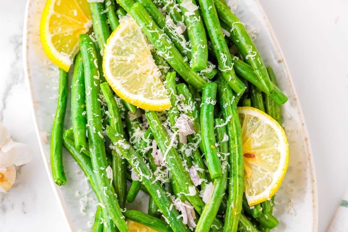 Green beans garnished with grated cheese and sliced lemon, served on a white oval plate.