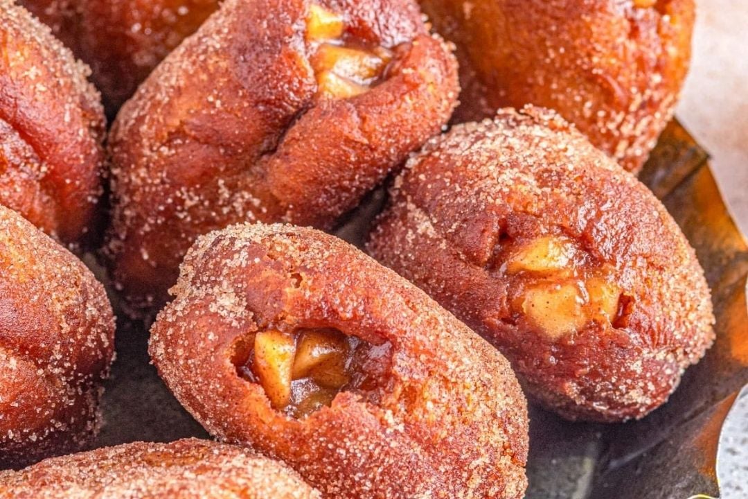 Close-up of several fried apple fritters coated in cinnamon sugar, with pieces of apple visible inside each pastry.