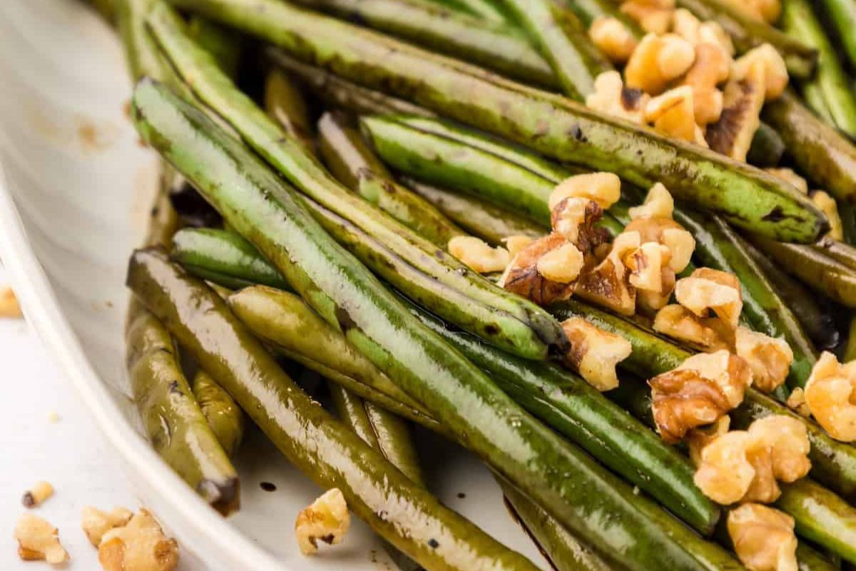 A plate of roasted green beans garnished with chopped walnuts.