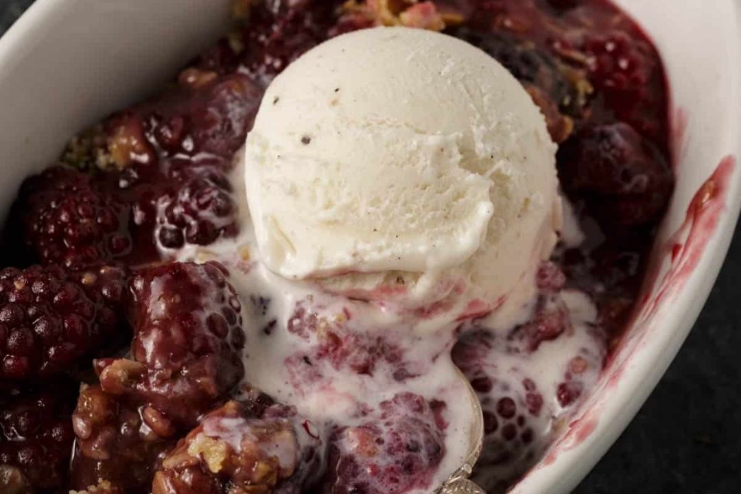 A scoop of vanilla ice cream melting over a serving of berry cobbler in a white dish, this easy recipe is the perfect way to enjoy homemade fruit cobblers.