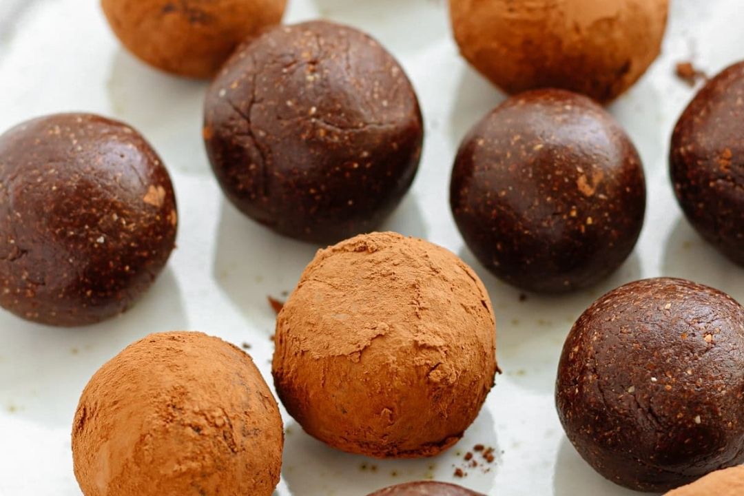 Several round chocolate truffles, some coated with cocoa powder and others with a glossy finish, are arranged on a white surface.