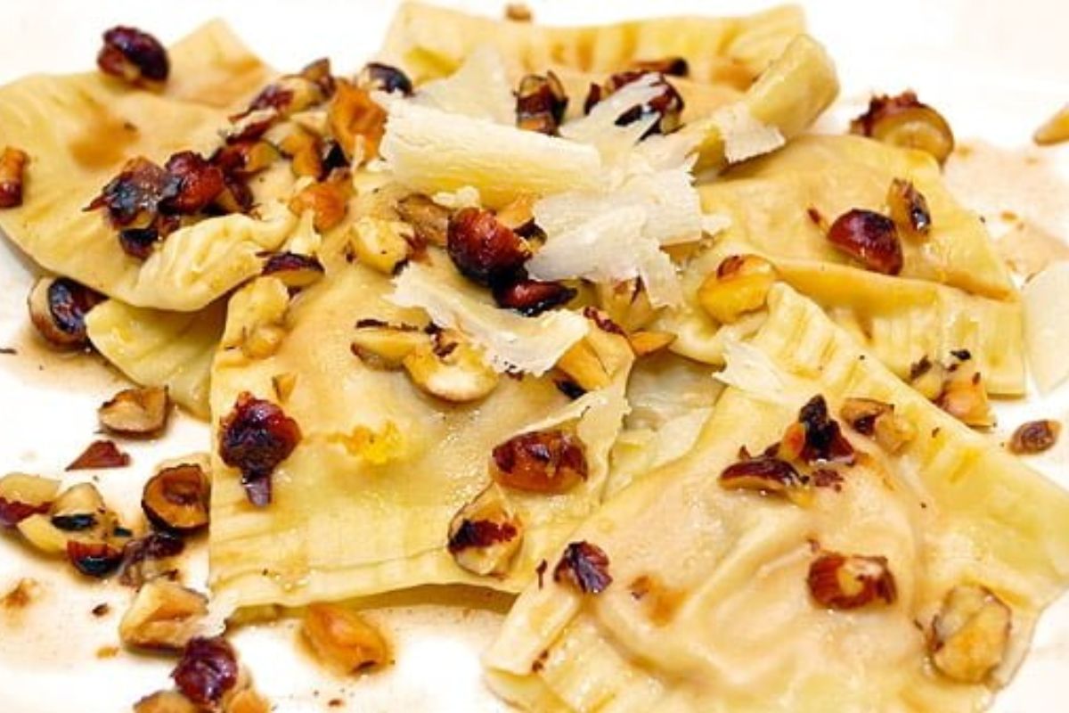 Ravioli topped with chopped toasted nuts and shaved cheese, served on a white plate.
