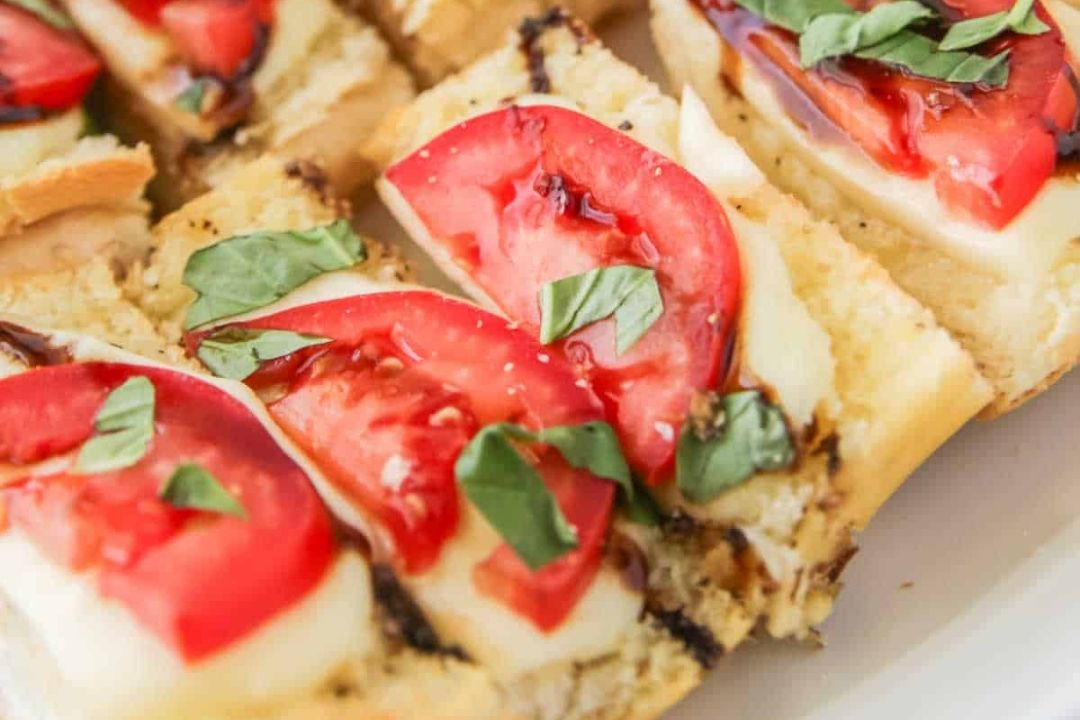 Close-up of sliced bread topped with peak tomato slices, mozzarella cheese, fresh basil leaves, and a drizzle of balsamic glaze—capturing the essence of summer flavor in every bite.