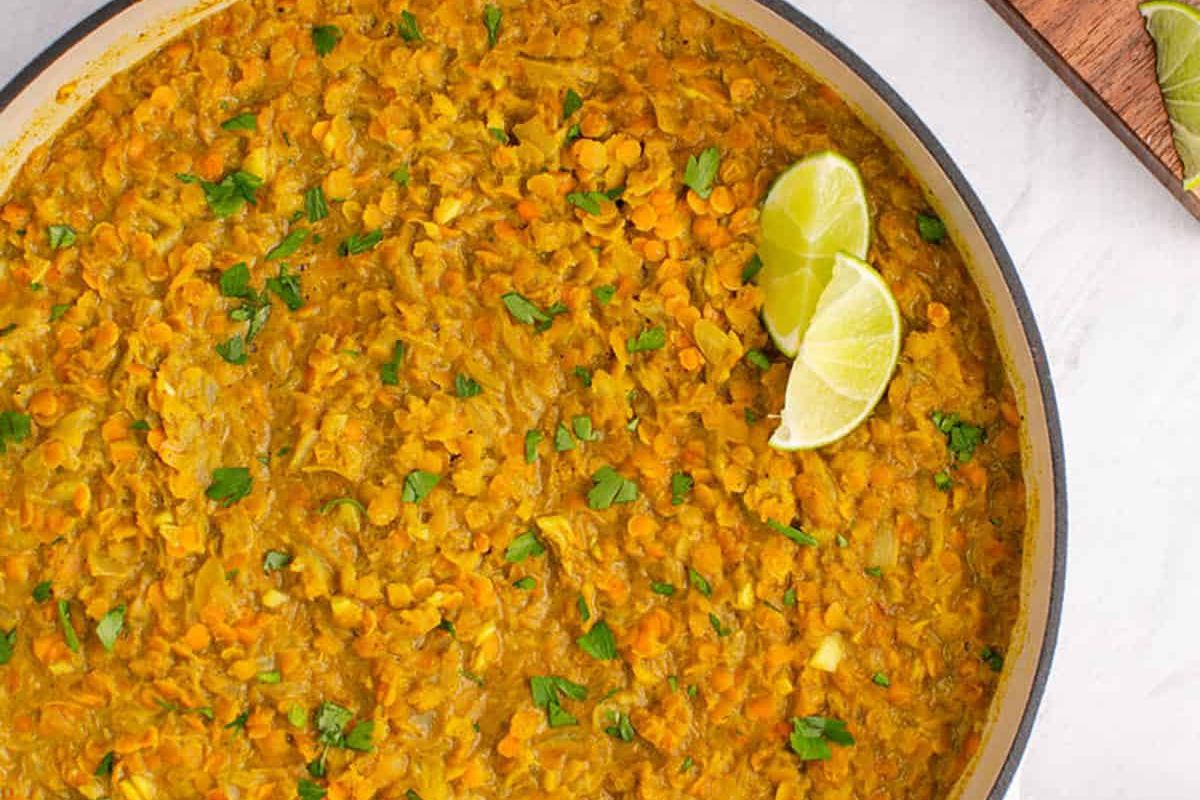 A pan of yellow lentil dal garnished with chopped cilantro and two lime wedges, viewed from above.