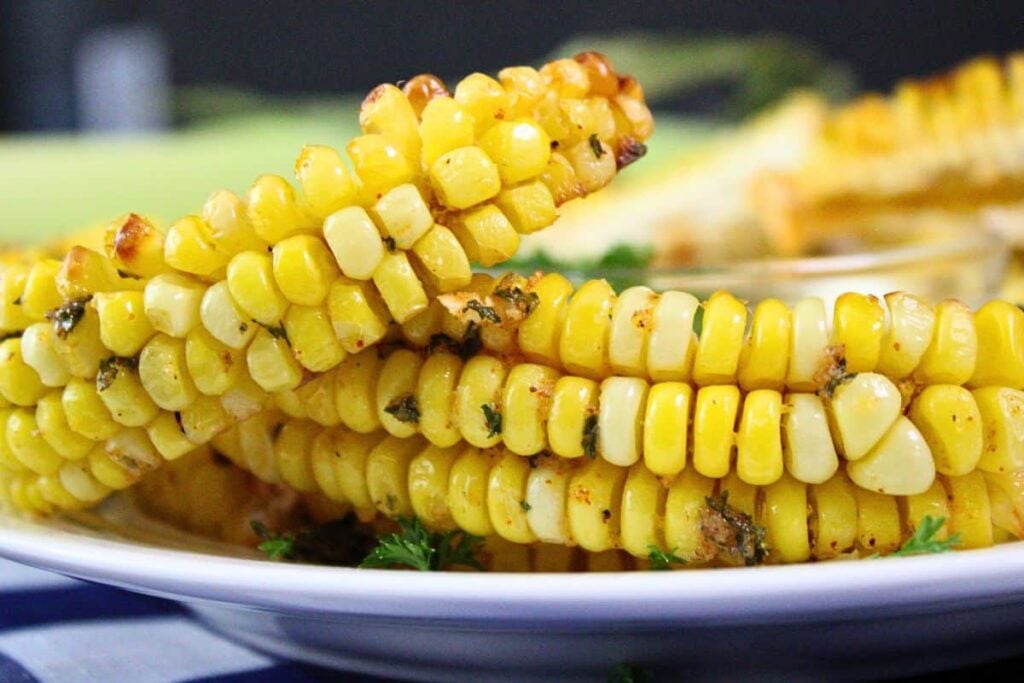 Close-up of grilled corn ribs arranged on a white plate, garnished with herbs.