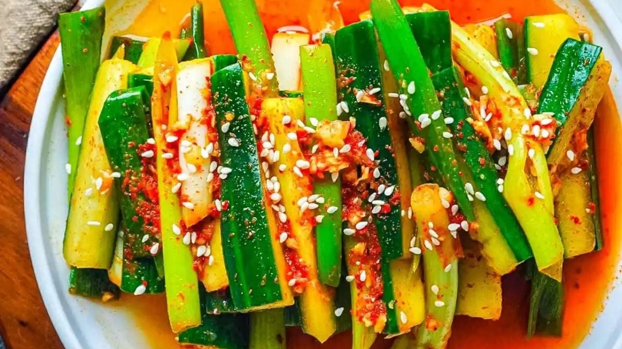 Plate of cucumber kimchi garnished with sesame seeds and red chili flakes, with green onions and a vibrant dressing.