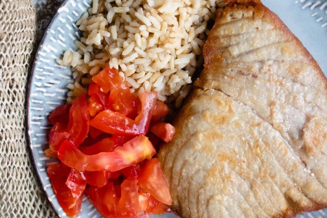 A plate with a grilled fish fillet, a serving of brown rice, and sliced tomatoes.