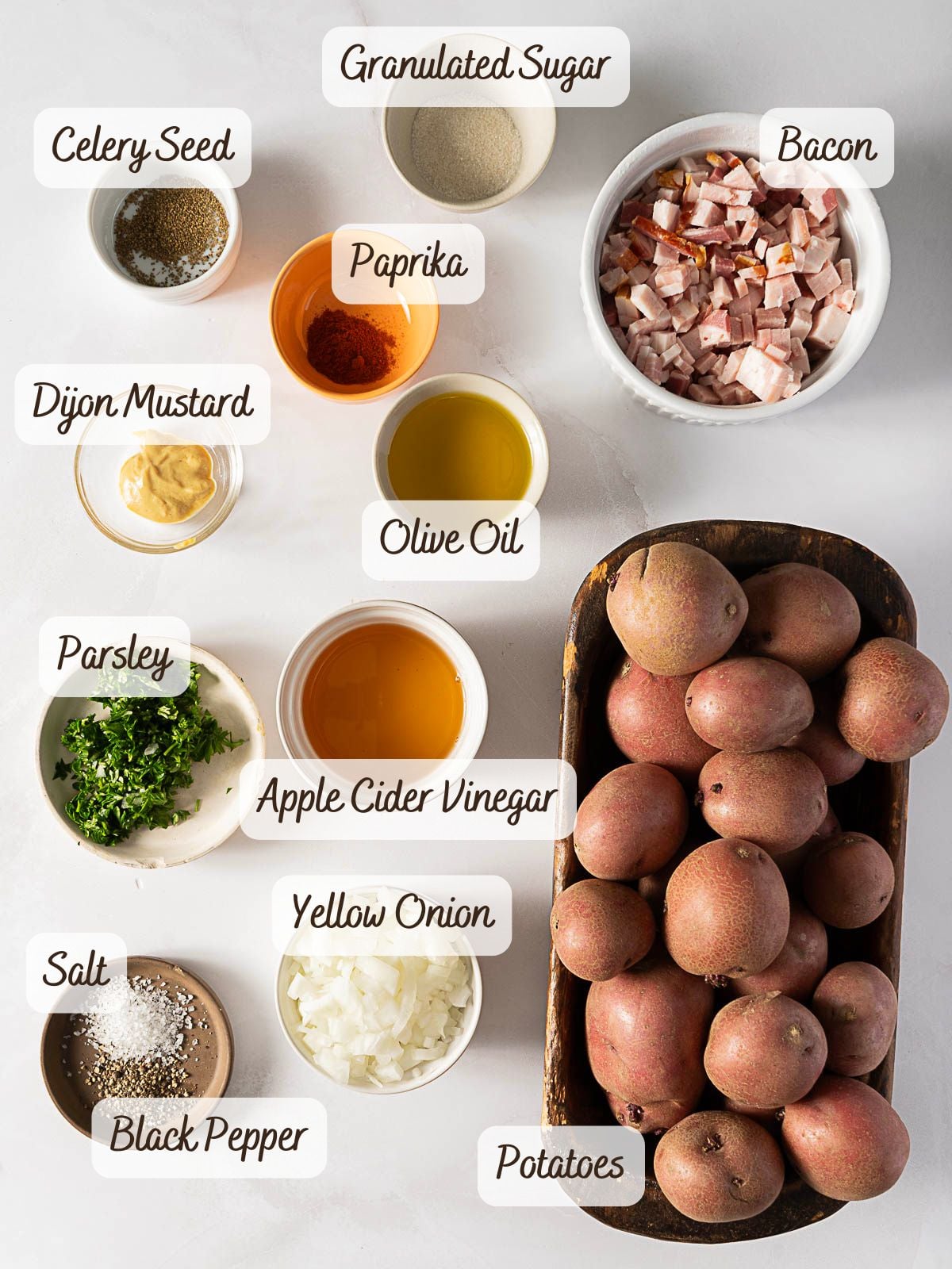 Ingredients for German potato salad, including potatoes, diced bacon, chopped onion, parsley, mustard, olive oil, apple cider vinegar, paprika, celery seed, sugar, salt, and black pepper.