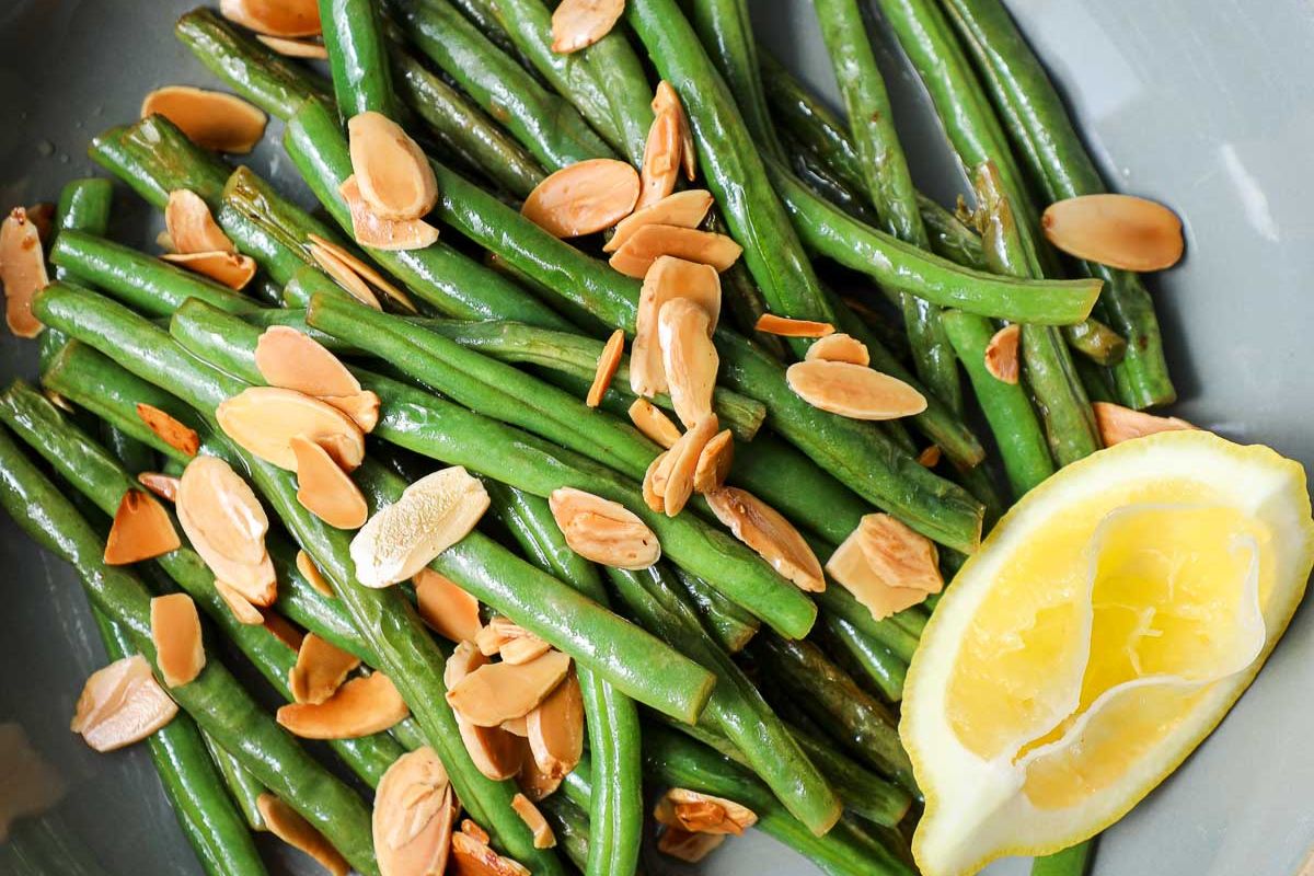 Green beans topped with sliced almonds, served with a lemon wedge on the side.