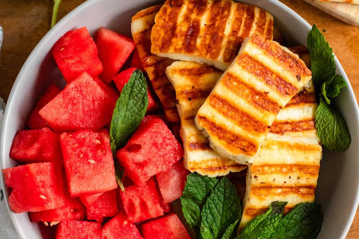 A bowl containing grilled halloumi slices, cubed watermelon, and fresh mint leaves.
