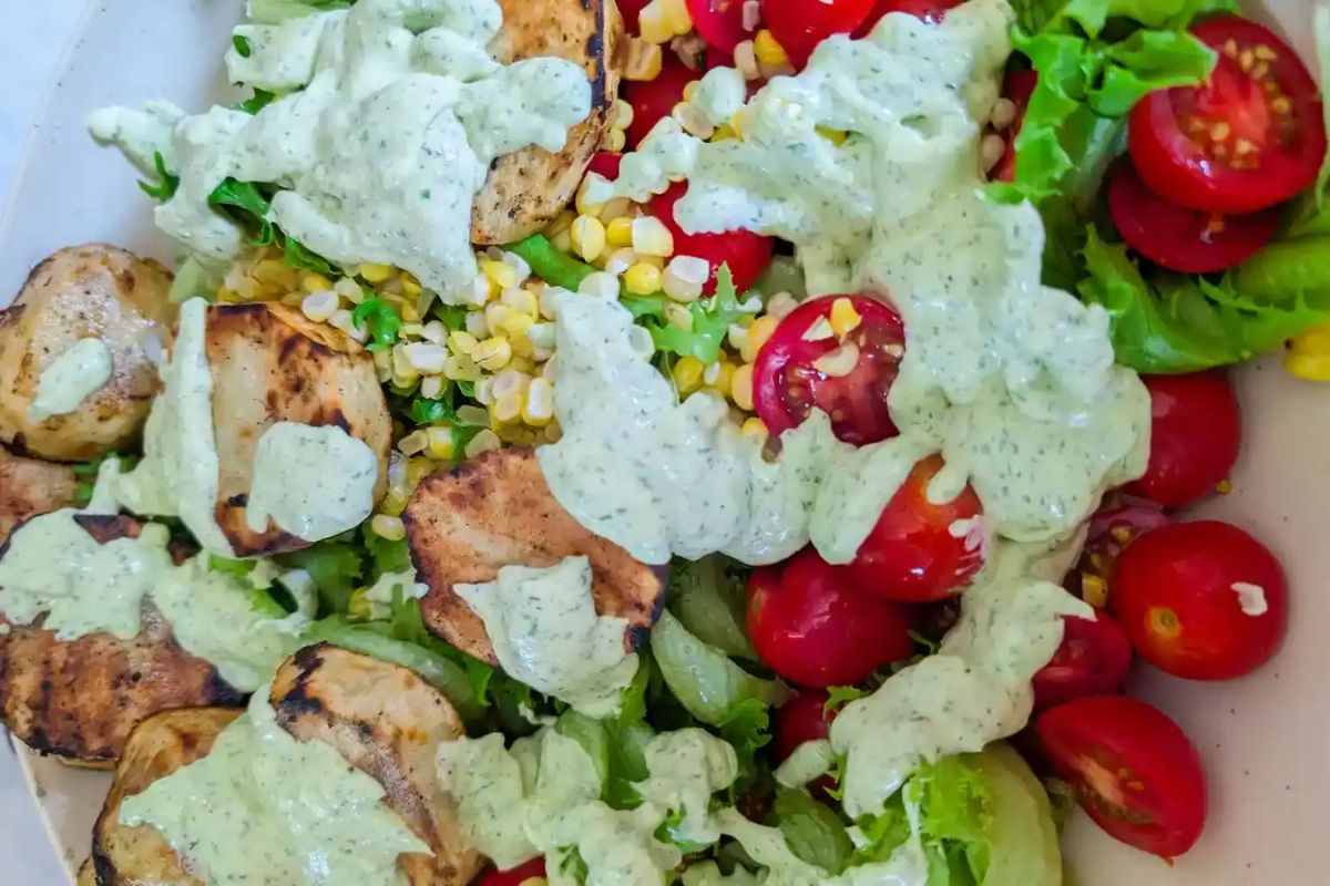 Salad with grilled chicken, cherry tomatoes, corn, lettuce, and a generous drizzle of creamy green dressing on top.