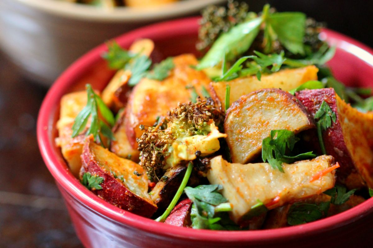 A red bowl filled with roasted vegetables including potatoes, broccoli, and fresh parsley.