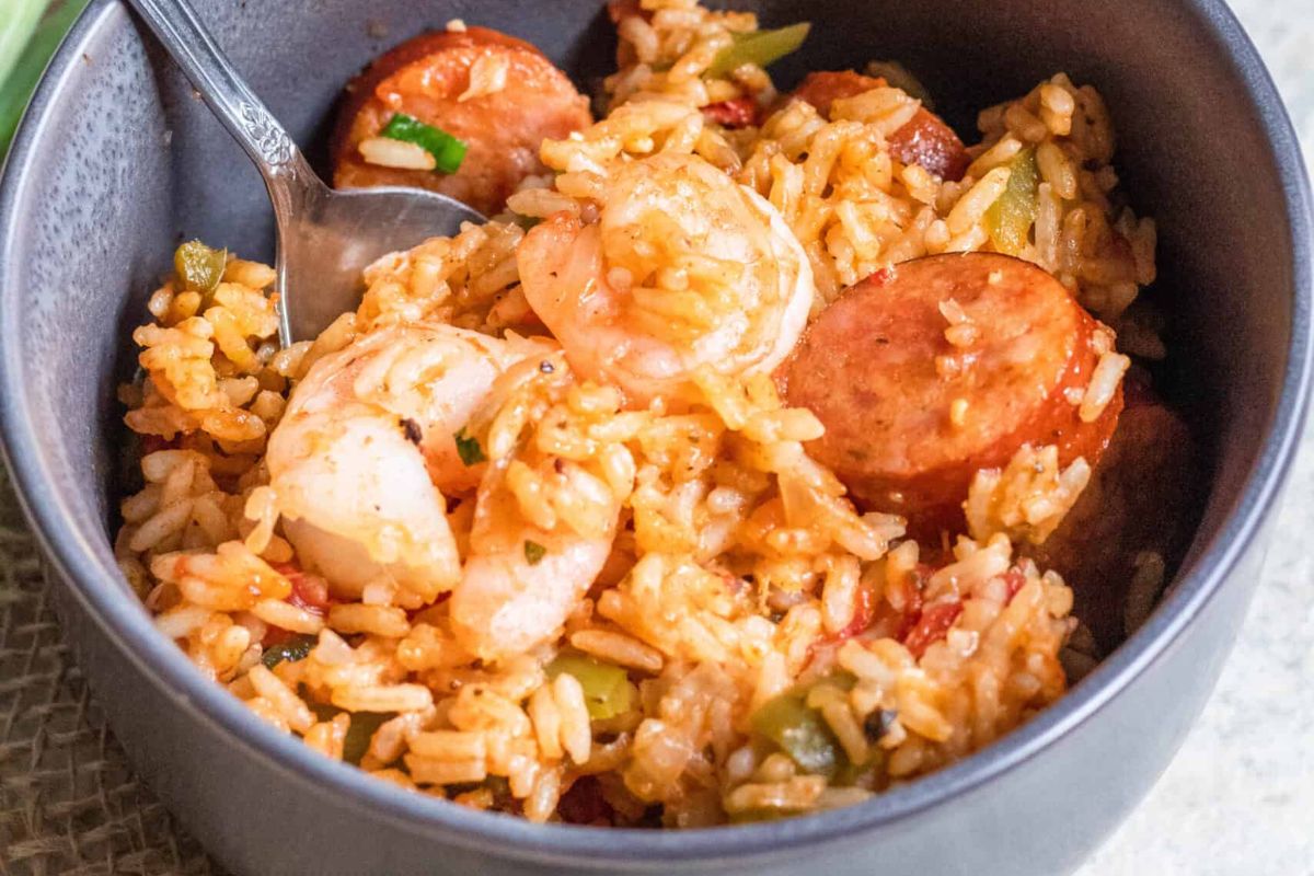 A bowl of jambalaya with shrimp, sausage, rice, and vegetables, served with a spoon.