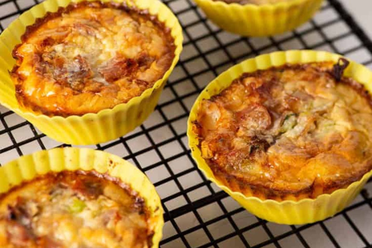 Four mini quiches in yellow silicone baking cups cooling on a black wire rack