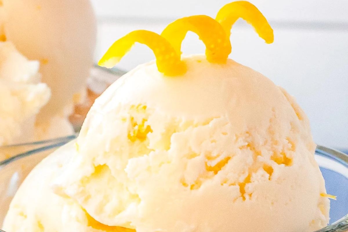 A scoop of vanilla ice cream topped with three small curls of orange zest, served in a glass bowl.