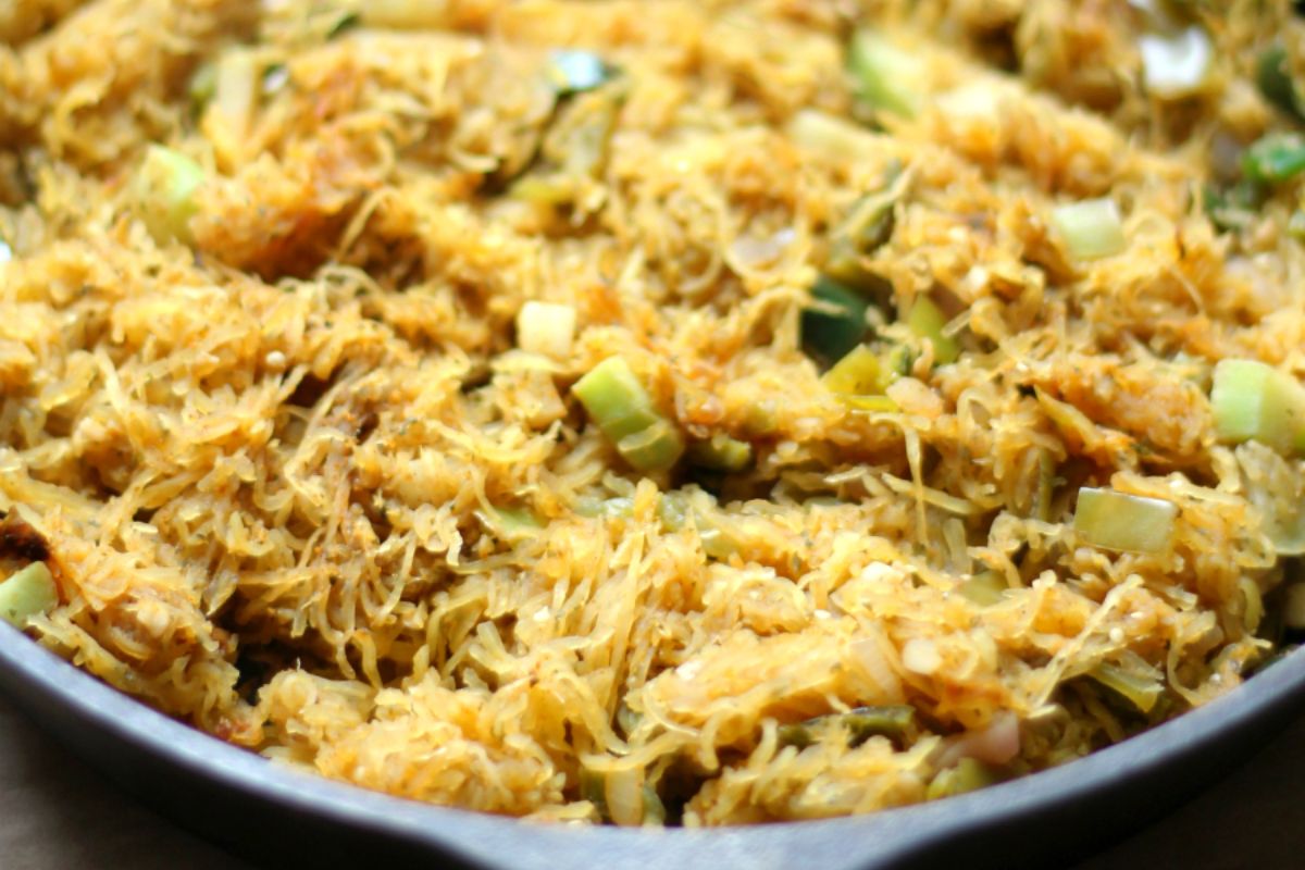 Close-up of cooked spaghetti squash mixed with chopped green vegetables and seasoning in a skillet.