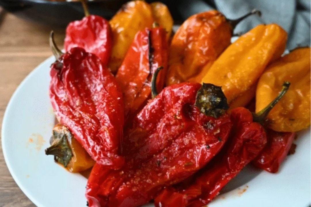 A white plate filled with roasted red and yellow peppers, with charred skins and visible seasonings.