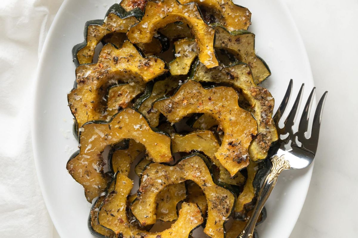 Slices of roasted acorn squash seasoned with spices are arranged on a white plate next to a serving fork.