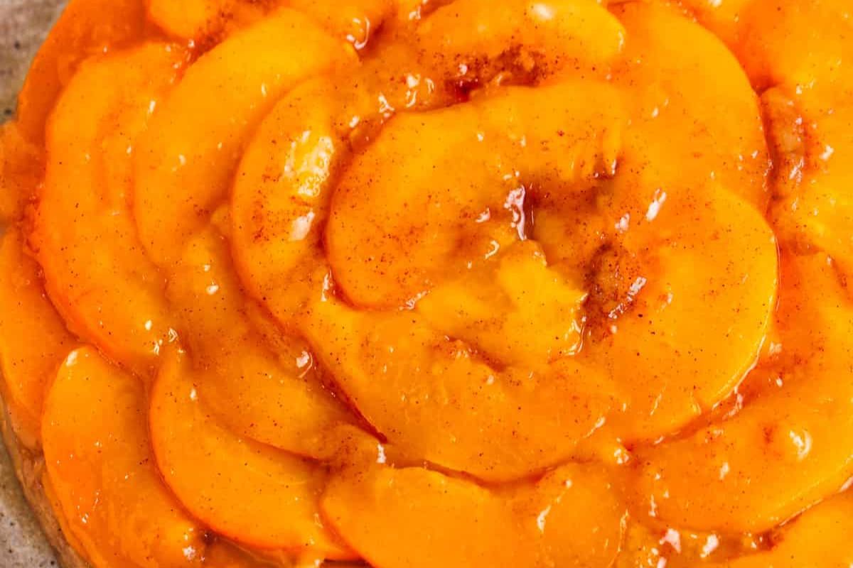 Close-up of glazed, sliced peaches arranged in overlapping layers, possibly on a tart or dessert, with a slight dusting of spices visible.