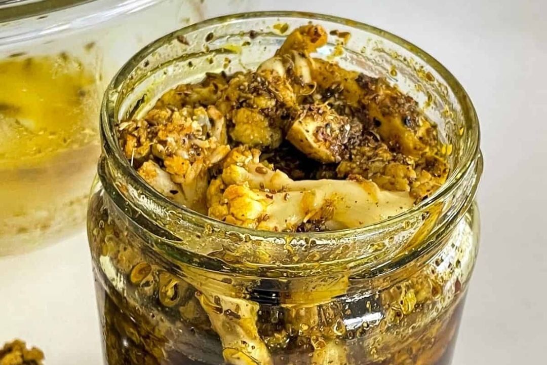 A glass jar filled with pickled cauliflower florets in a dark, spiced liquid.