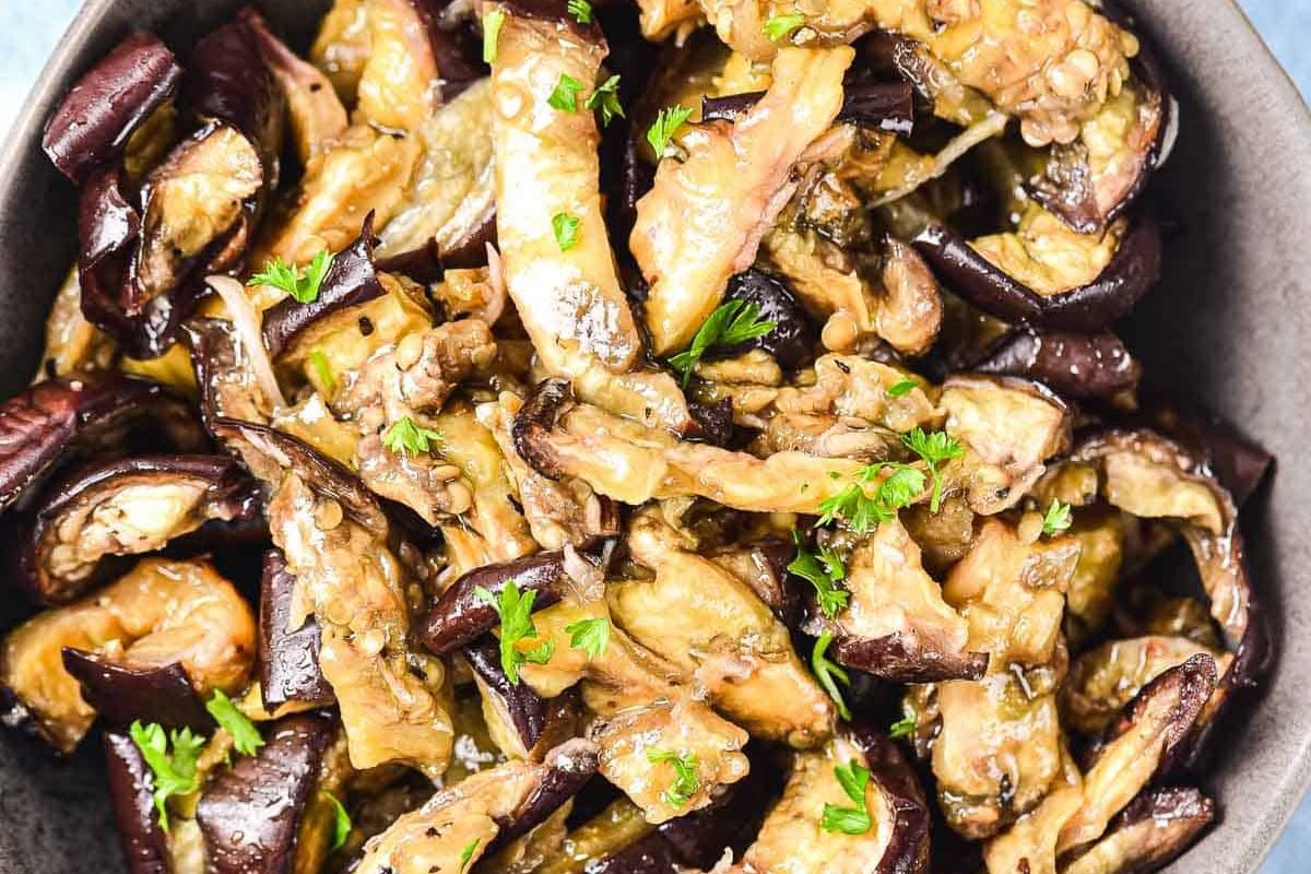 A bowl of roasted eggplant pieces garnished with chopped fresh parsley.