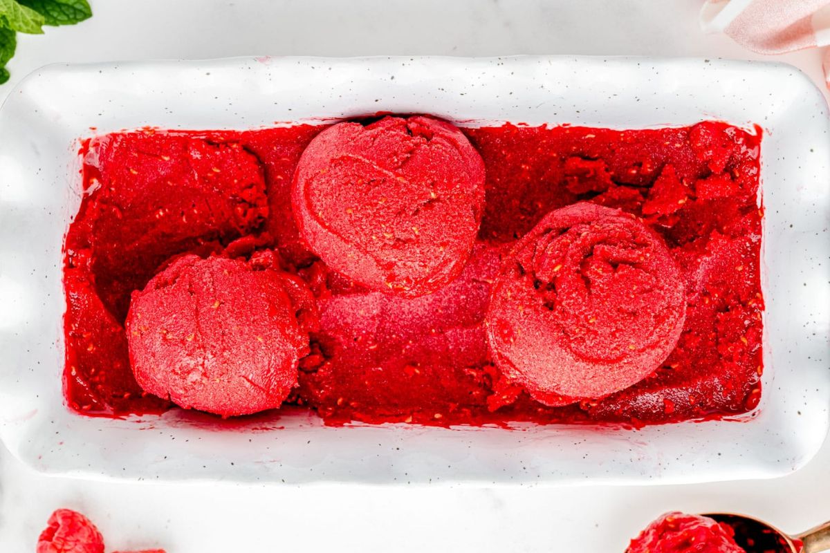 Rectangular white dish filled with bright red sorbet, with three round scoops on top and more sorbet visible around them.