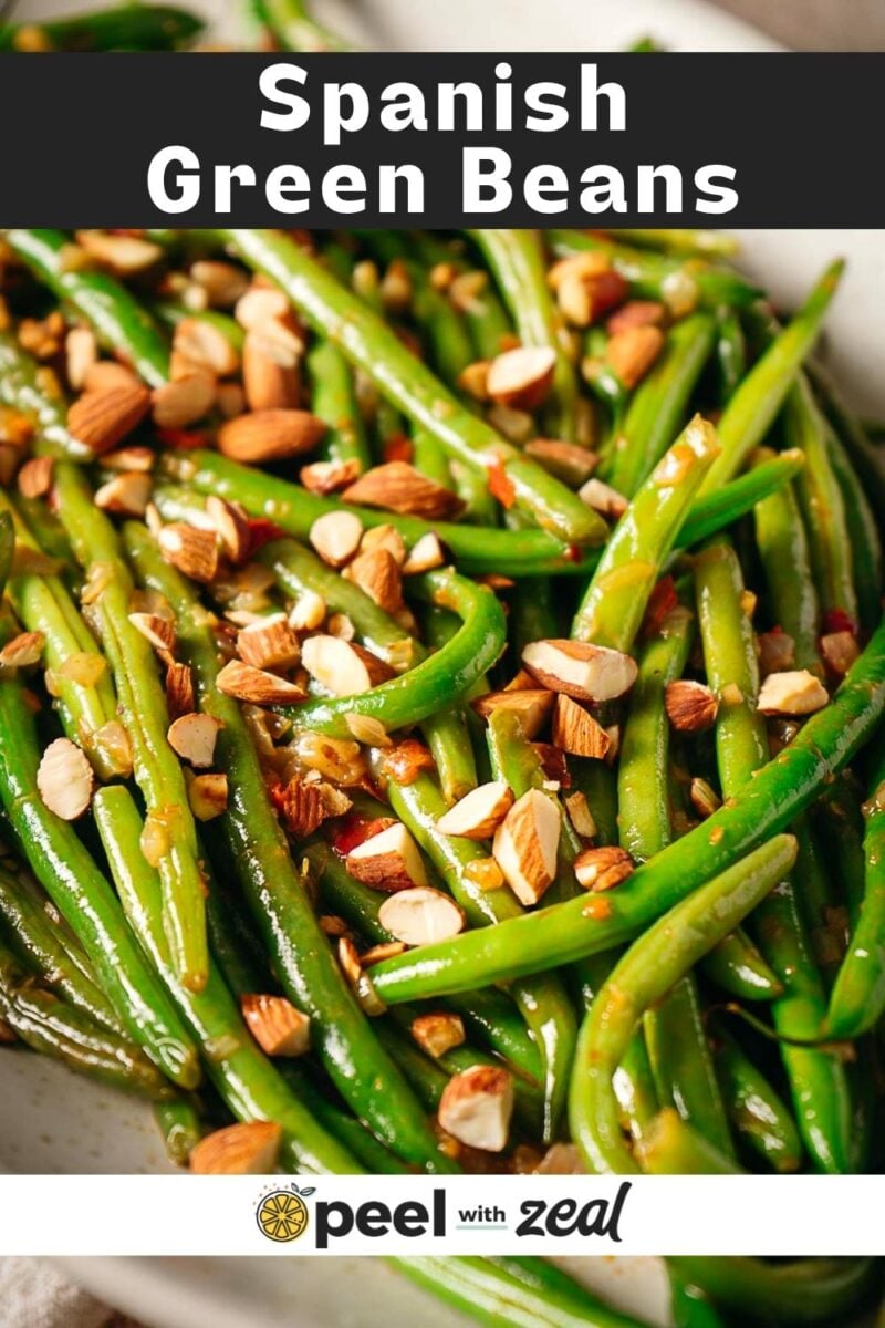 Cooked green beans topped with chopped almonds, served on a white plate. Text at the top reads "Spanish Green Beans" and a logo at the bottom says "peel with zeal.