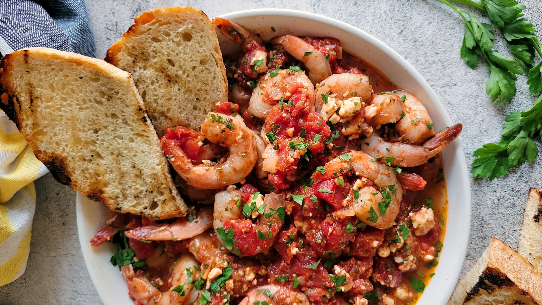 A bowl of shrimp in tomato sauce made from extra garden tomatoes, garnished with herbs and served with two slices of toasted bread on the side.