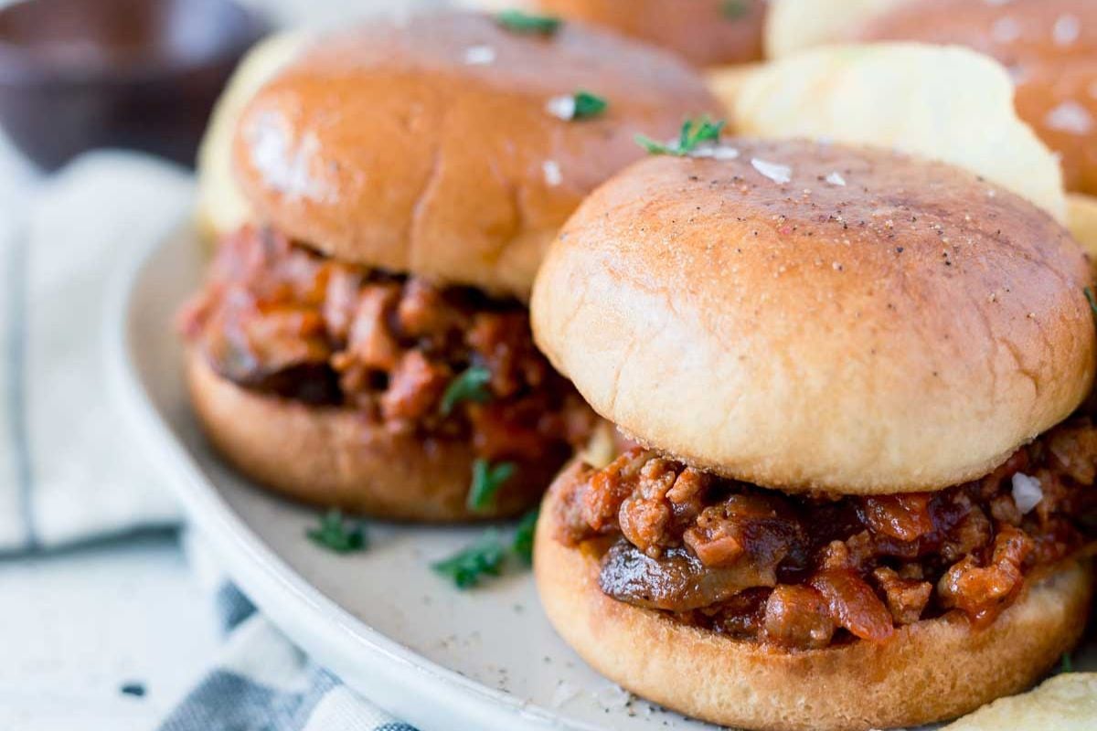 Close-up of two sloppy joe sandwiches with saucy ground meat filling on toasted buns, served on a white plate.