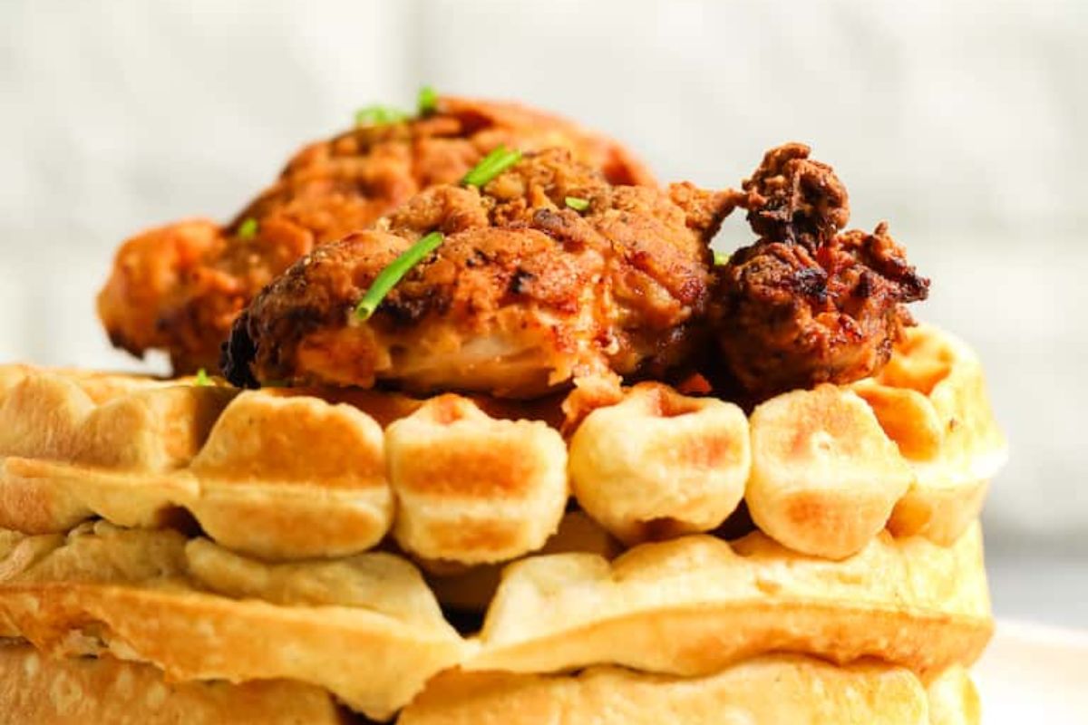 Two pieces of fried chicken are served on top of a stack of waffles, garnished with small green herb pieces.