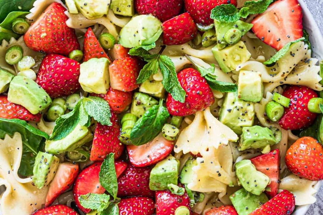 Bowtie pasta salad with strawberries, avocado, green onions, spinach, poppy seeds, and fresh mint leaves, all mixed together.