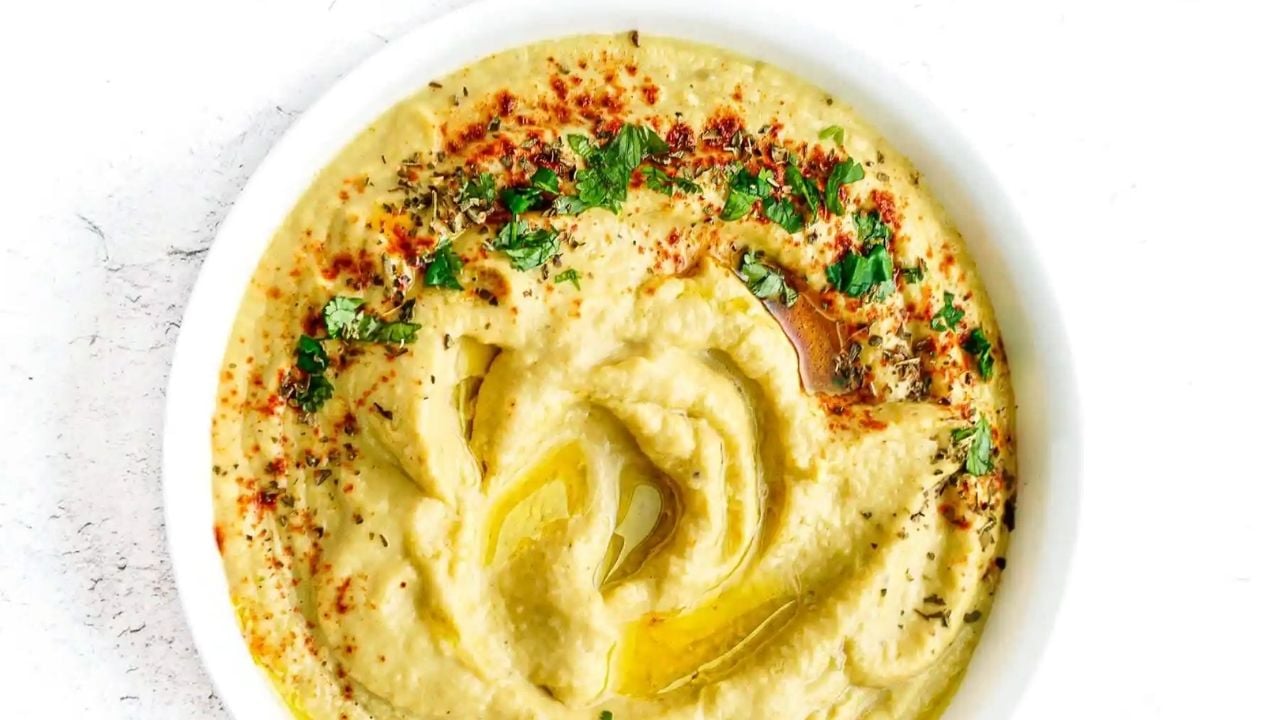 A bowl of hummus garnished with chopped parsley, paprika, dried herbs, and a drizzle of olive oil.