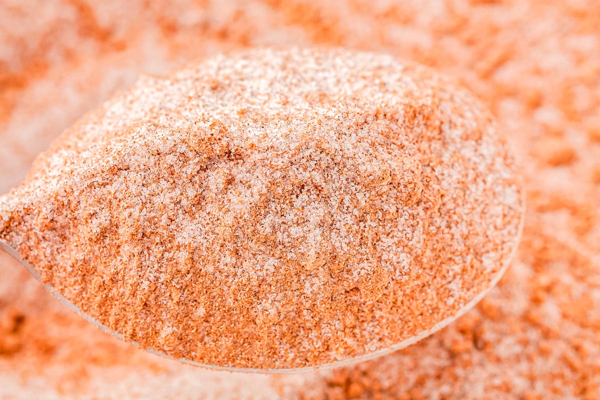 A close-up of a spoonful of reddish-brown seasoned salt, perfect for enhancing your favorite seasonal recipes, with more seasoned salt blurred in the background.