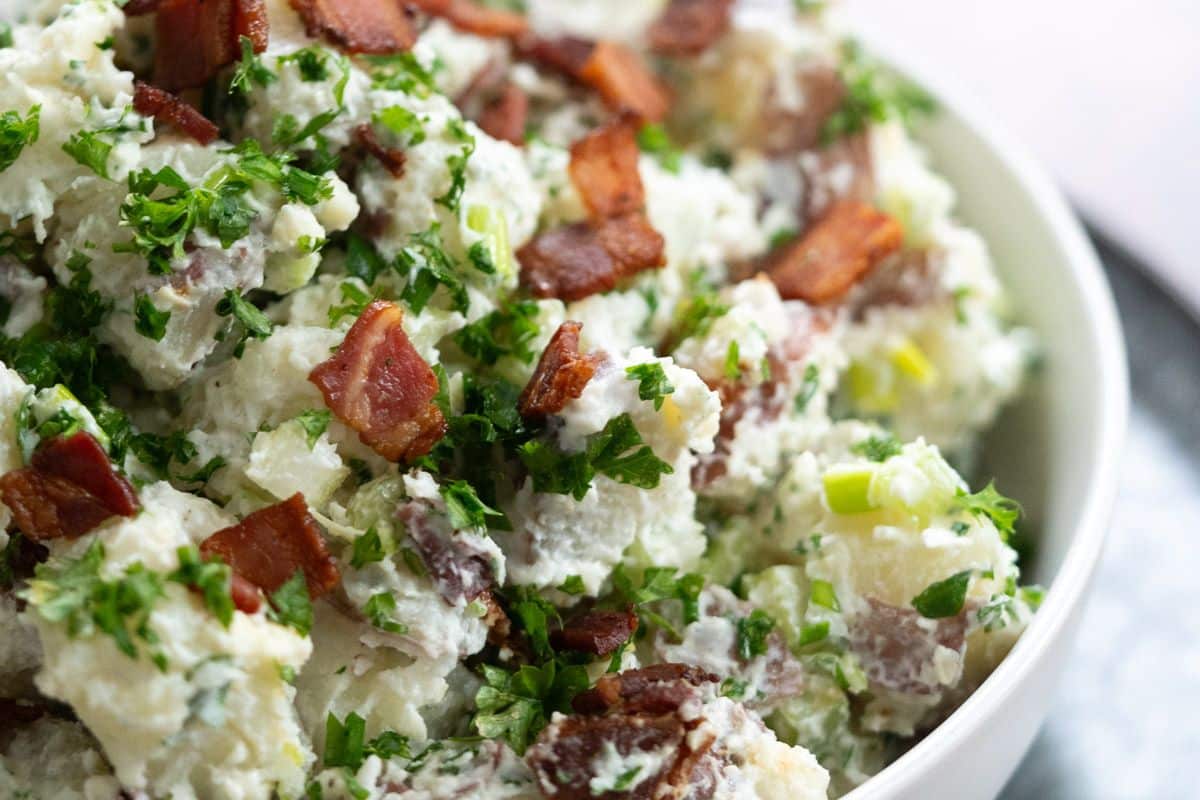 A bowl of potato salad topped with chopped bacon, fresh parsley, and green onions—one of our reader favorites when it comes to crowd-pleasing side dishes.
