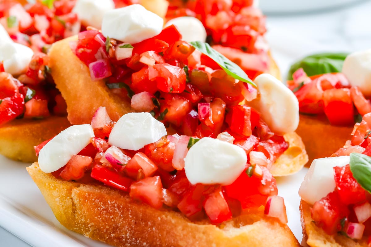 Garden-Fresh bruschetta topped with diced tomatoes, red onions, basil, and small mozzarella pieces on toasted bread slices.