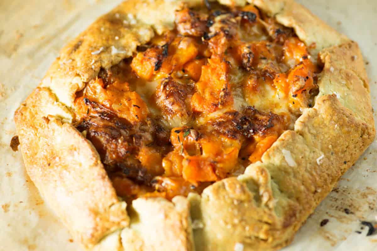 A rustic galette with a golden, flaky crust filled with roasted orange vegetables and melted cheese, baked until lightly browned—perfect for autumn meals or anyone seeking comforting fall recipes.