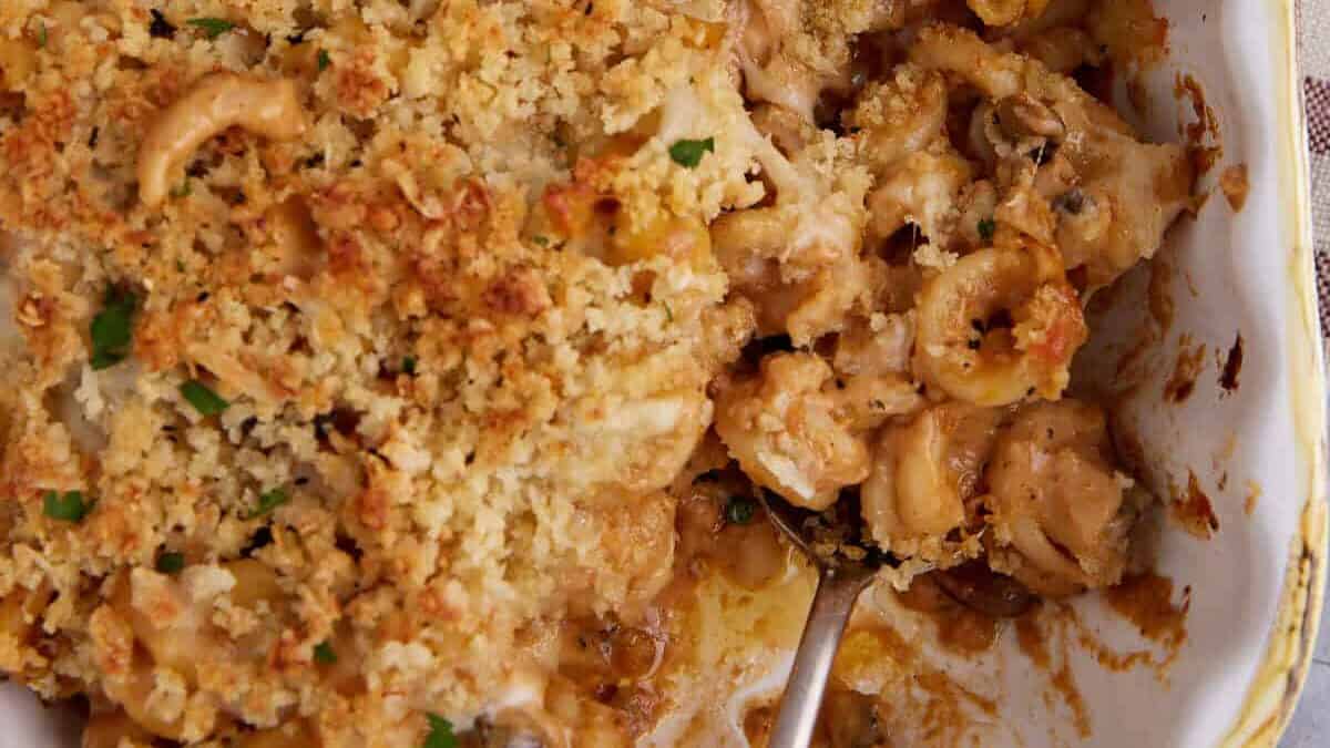 A baked casserole with a golden breadcrumb topping and creamy filling, partially scooped out with a metal spoon—perfect for cozy pasta dinners.