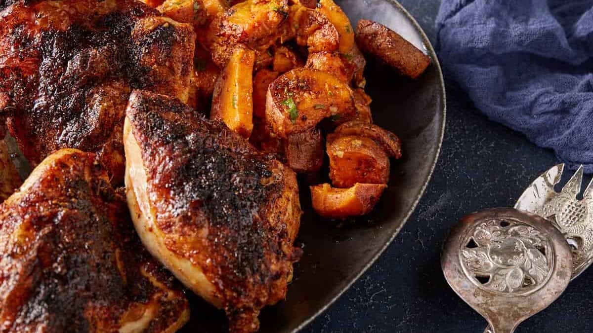 Roasted chicken breasts and thighs with beautifully browned skin, served on a black plate alongside roasted potatoes and mushrooms—a perfect choice for those seeking delicious new chicken dishes.