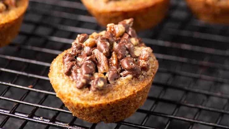 Close-up of a baked cookie cup filled with chopped pecans and melted chocolate, reminiscent of decadent chocolate chip treats, resting on a black wire cooling rack.