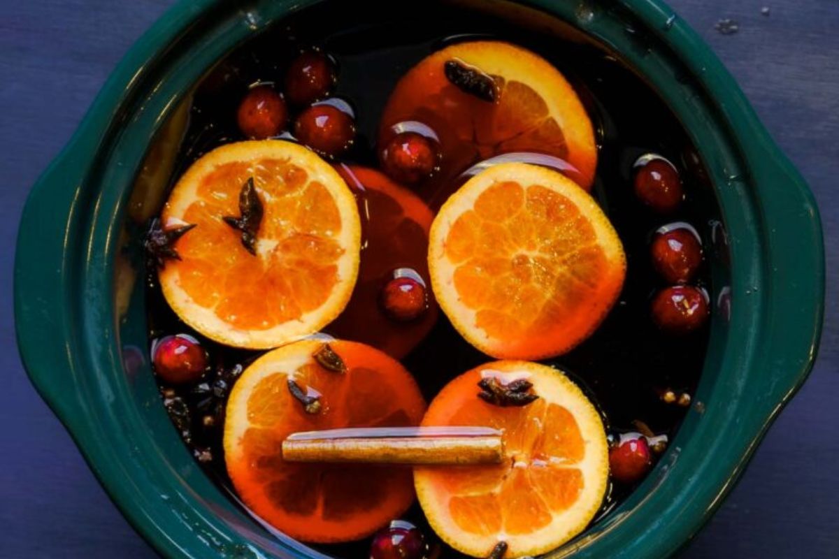 A slow cooker filled with sliced oranges, cranberries, spices, and a cinnamon stick in dark liquid—this comforting scene captures the essence of cozy fall recipes and classic Crockpot recipes perfect for chilly days.