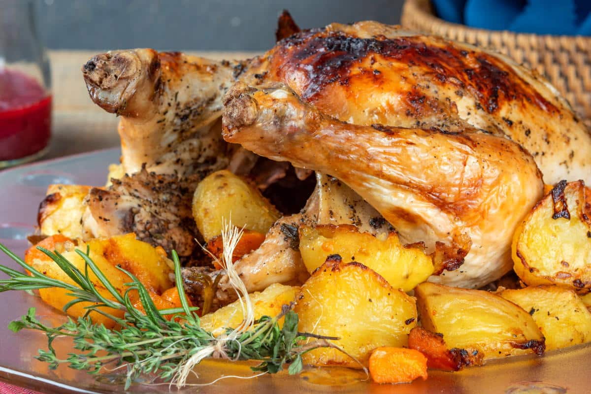 Roast chicken with golden, crispy potatoes and fresh herbs served on a platter—perfect for anyone looking for delicious roasted chicken recipes.