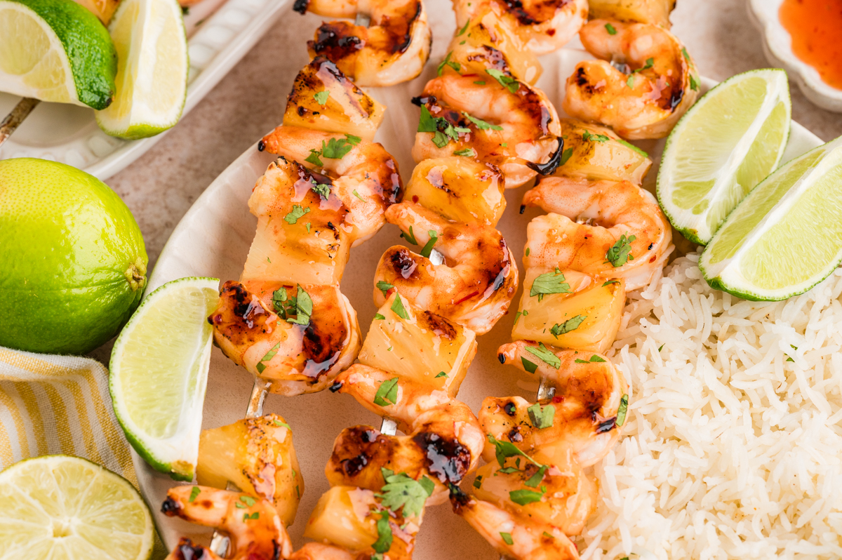 Grilled shrimp and pineapple skewers garnished with herbs, served with white rice and lime wedges on a plate—a vibrant addition to your collection of summer recipes and perfect for any Labor Day cookout.