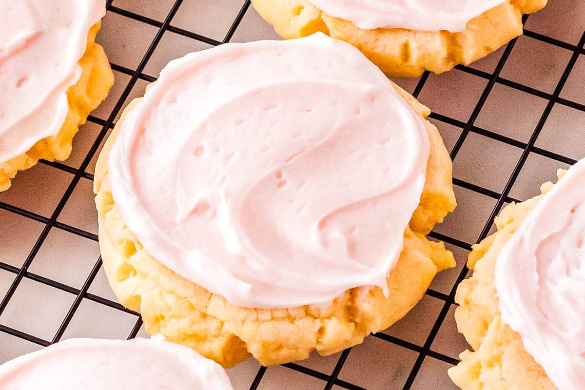 A round sugar cookie with pink frosting sits on a black wire cooling rack, making it a perfect easy dessert for summer cookouts or Labor Day gatherings, with parts of two other cookies visible nearby.
