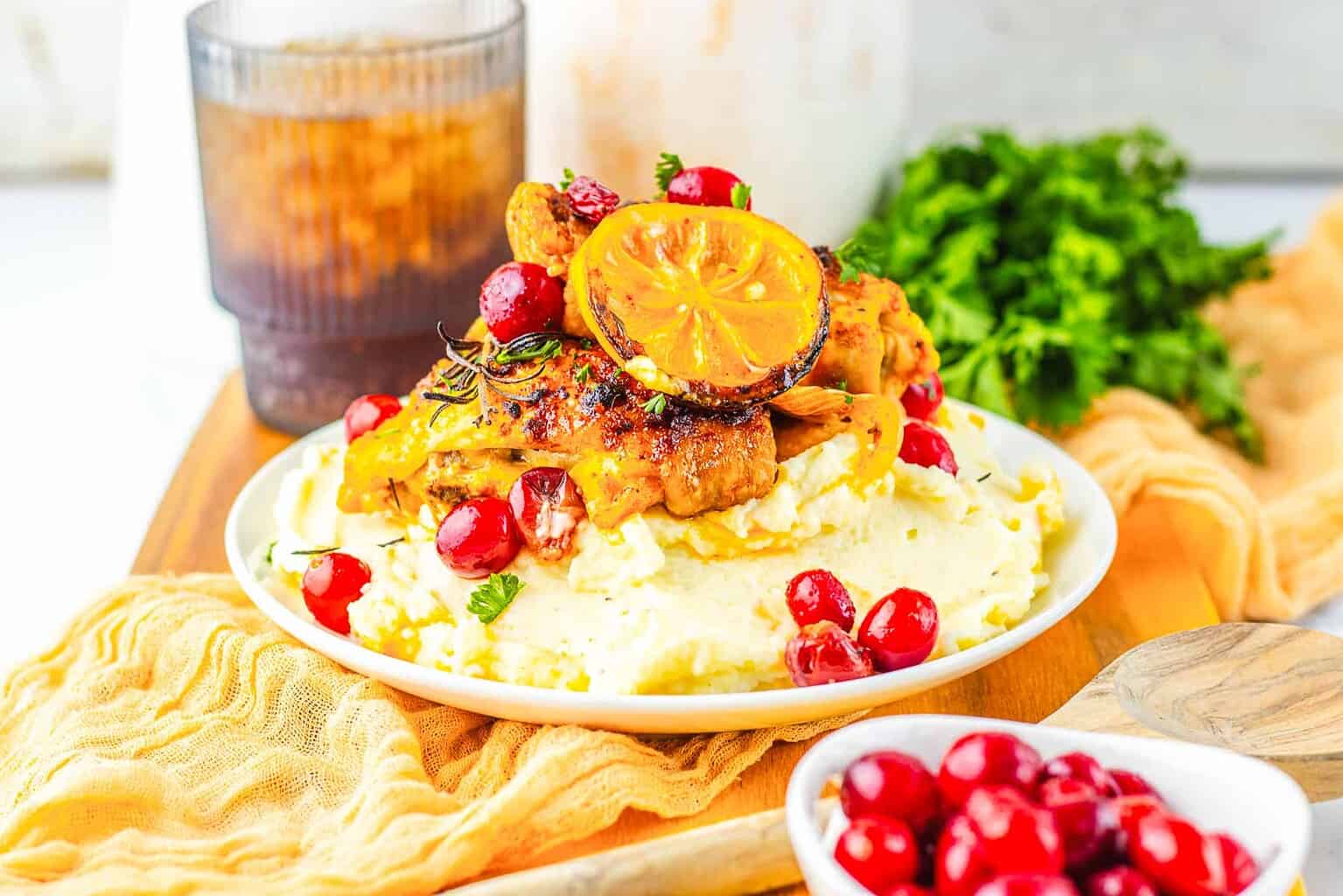 Grilled chicken with a slice of lemon on mashed potatoes, garnished with fresh herbs and cranberries, served with a drink and a side of cranberries—an inspired twist on classic roasted chicken recipes.